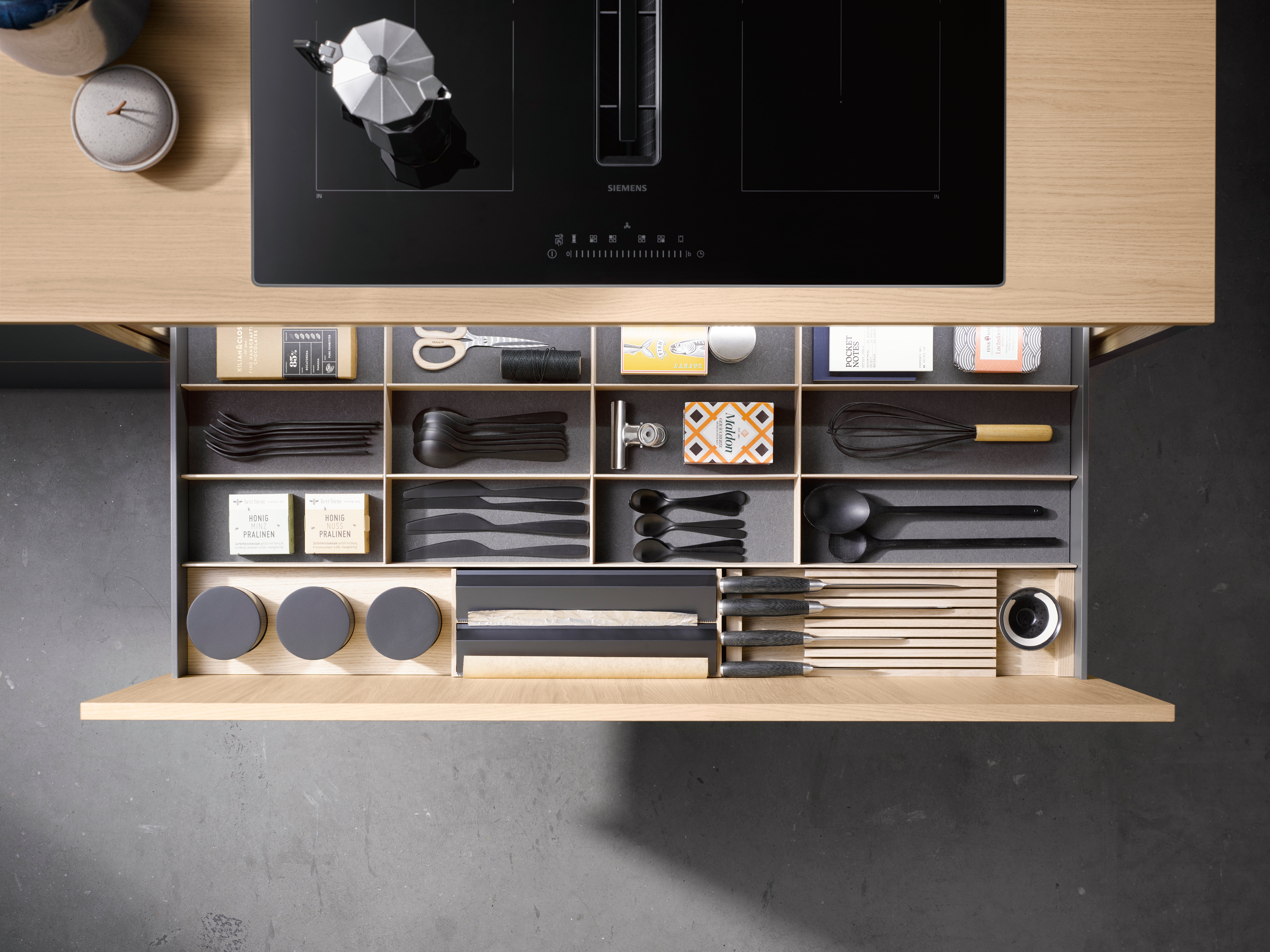 Offene Küchenschublade mit geordnetem Besteck, Gewürzen und Kochutensilien.