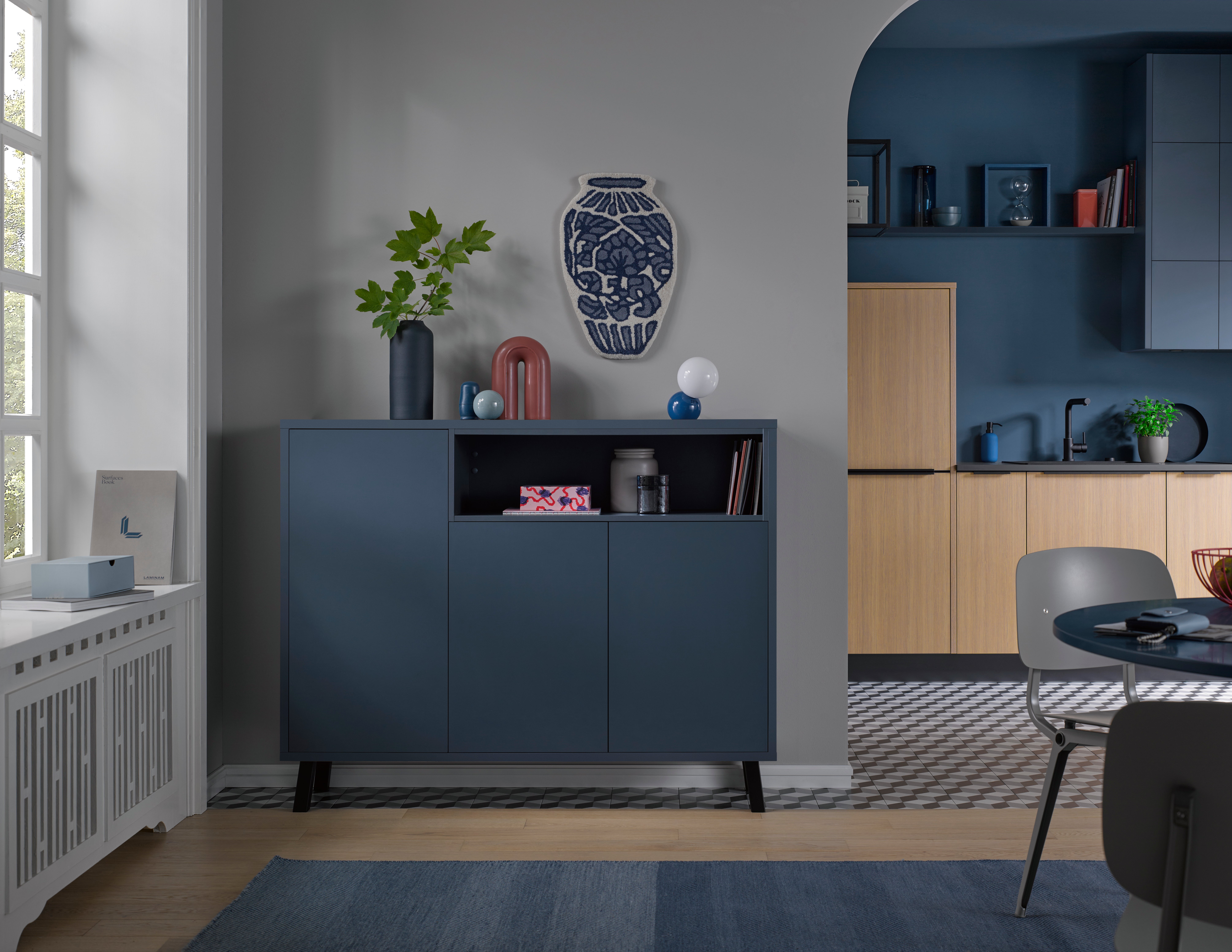 Modernes Wohnzimmer mit blauem Sideboard, Dekorationen und angrenzender offener Küche.