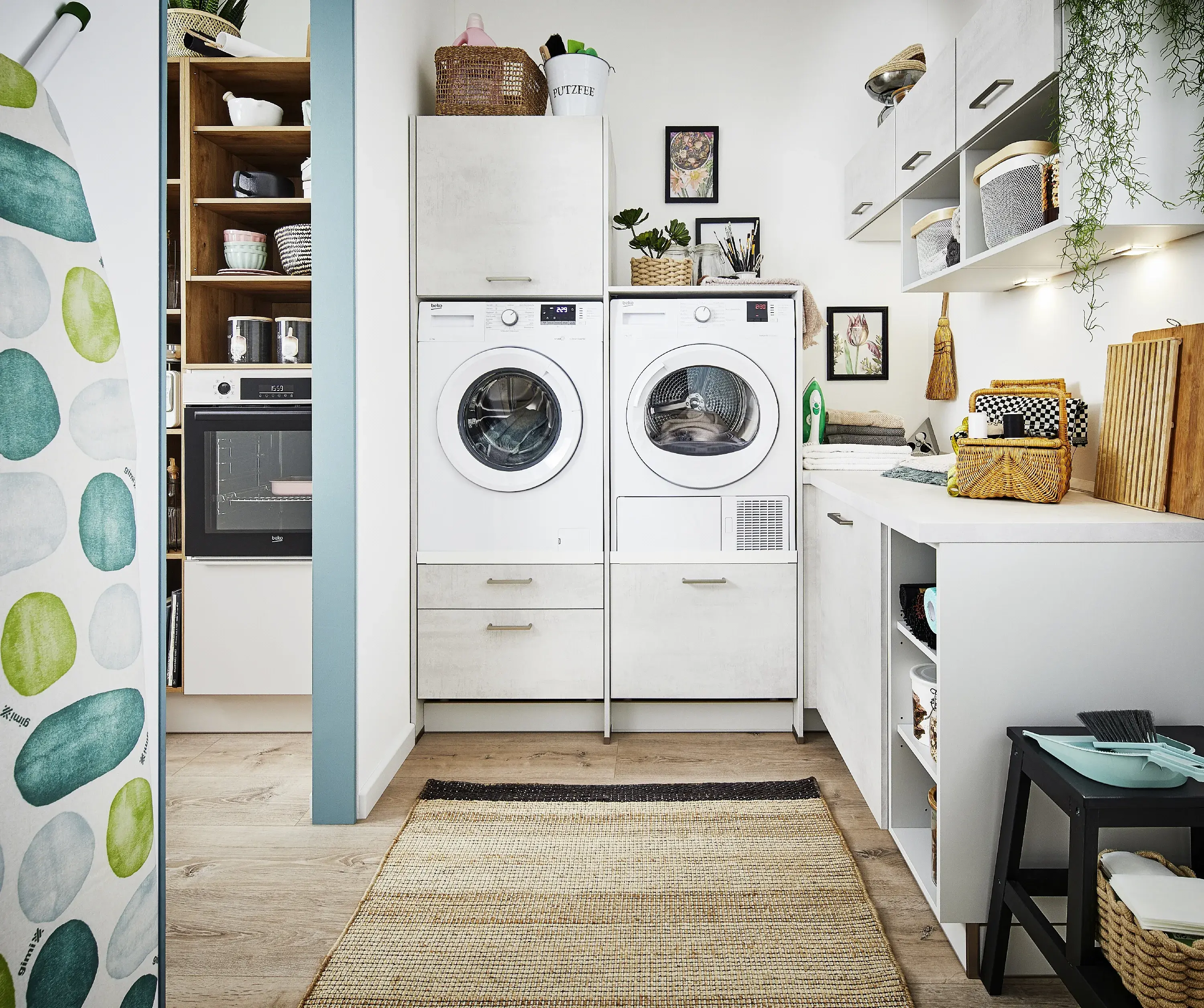 erhöht eingebaute Waschmaschine daneben Trockner im Hauswirtschaftsraum angrenzend an die Küche getrennt durch dünne Rigipswand